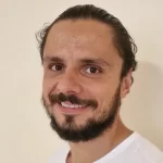 Un bărbat cu barbă zâmbește la cameră la curs instructor de Yoga Brașov